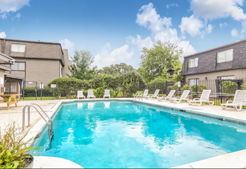 Blue pool with lounge chairs on 2 sides.  Buildings surrounding.